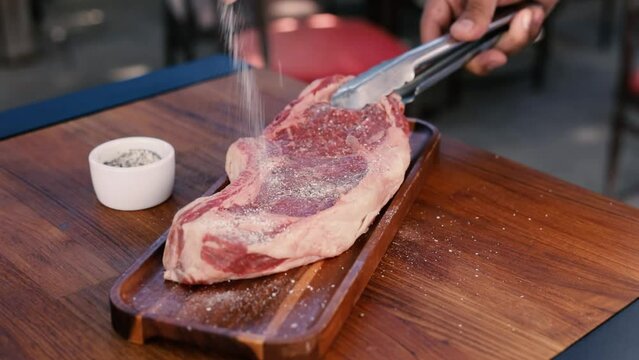 Person seasoning steak with salt and pepper panning