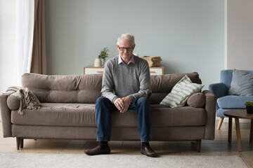 Upset thoughtful retired single man sit on couch alone, feels abandoned, suffer from weakness,...