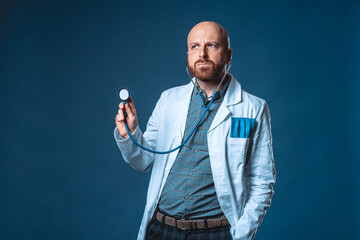 Photo of doctor with beard and stethoscope posing listening with blue background and medical white coat