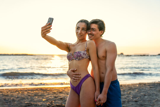 lifestyle photoshoot of young helthy beautiful caucasian couple, active boy and girl, dating at the beach - Man and woman lovers having fun in holidays taking selfies near the ocean in a sunny day