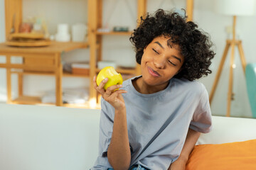 Happy pretty girl biting green apple at home. Beautiful african american young woman eating fresh fruit and smiling. Healthy food vegan vegetarian dieting concept. Healthy snack clean food