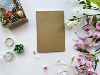 
Romantic floral background with tiny pale pink flowers, succulents and candles sprinkled on white background, with notebook copy/space for your text