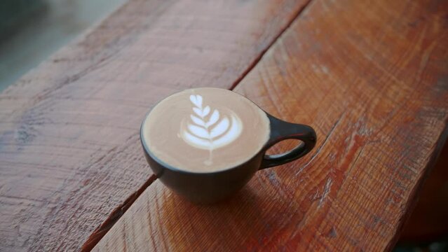 Handheld parallax of latte art in black teacup with white leaves at cafe