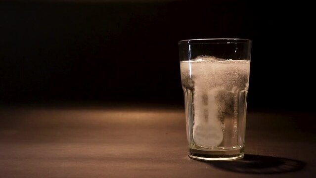 Effervescent tablet falling in a glass of water on black background in a muffled light. Taking medication concept. Taking calcium, magnesium, vitamins, aspirin for a healthy life.