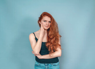 Fototapeta premium Dreamy woman with long red hair in a black tank top on a gray background. Hand near face.