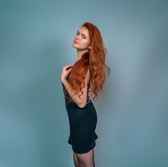Profile of a girl with big brown eyes. Looks into the camera. Long red hair, black dress. Gray background.