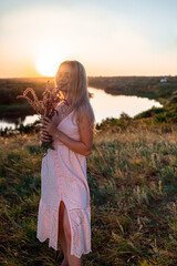 Happy young woman with wildflowers on nature background in summer at sunset. female is relaxing in the field with flowers. Soft golden color