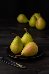 Close-up of three wet green pears on black plate, with four more in the background, selective focus, black background, vertical, with copy space