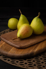 Top view of four wet green pears on wooden boards, selective focus, black background, vertical, with copy space