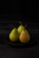 Top view of three green pears on black plate, black background, vertical, with copy space