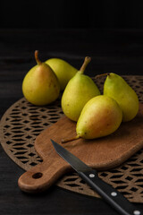 Top view of five green pears on wooden boards and knife, selective focus, black background, vertical, with copy space
