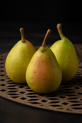 Close-up of green pears on trellis and wooden table, selective focus, black background, vertical, with copy space