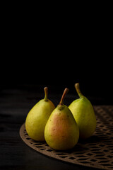 Top view of green pears on trellis and wooden table, selective focus, black background, vertical, with copy space