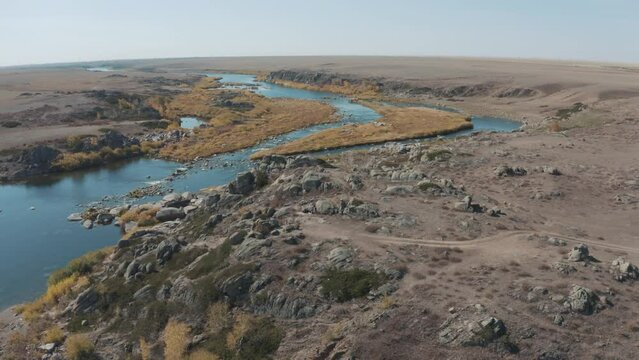 This stock video shows a beautiful landscape: a winding river with a rocky bottom, plains and banks, yellow grass and blue sky. This video will decorate your projects related to nature, weather.