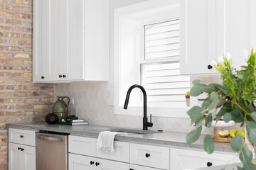 A beautiful kitchen sink detail with white cabinets, marble countertops, and a hexagon tiled...