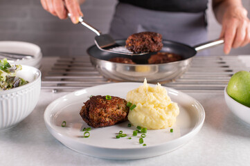 Woman with apron serving or putting meatballs from a frying pan on a plate