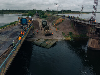 Fototapeta na wymiar Pontoon bridge of the Ukrainian army. Installation of a temporary crossing near the destroyed bridge. Soldiers collect pontoon ferry. Top view from a drone. Nikopol, UKRAINE – May 26, 2020