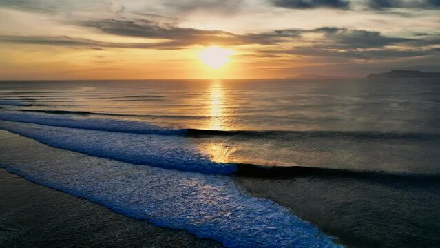 Drone clip showing perfect waves breaking at bright golden sunset in Java, Indonesia.