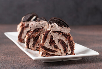 Sliced chocolate meringue roll with cookies on white plate on brown background, Closeup