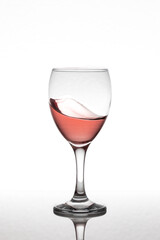 Motion glass of rose wine isolated on a white background over a reflective surface.