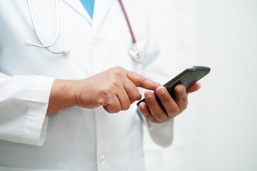 Asian woman doctor holding mobile phone or tablet for search method of treatment patient in...