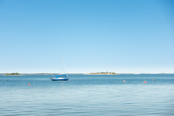 Fototapeta premium Sailboat anchored in crystal clear turquoise water in a tropical bay with vast blue sky in Stockholm archipelago for summer sailing holiday