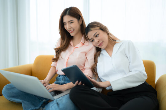 LGBT couple sitting on sofa and using laptop computer at home. - Powered by Adobe