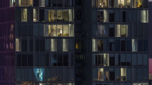Frontal view of night facade of tower building with a lot of blinking windows with light timelapse. Life in every window. Aerial view of the glass facade of residential skyscraper.