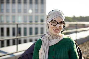 Portrait of smiling muslim woman wearing traditional clothing using hands-free headset on panoramic...