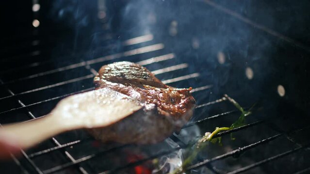 Close-up turning grilled meat on bbq with spatula in slow motion. High angle view closeup delicious meal grilling on barbecue