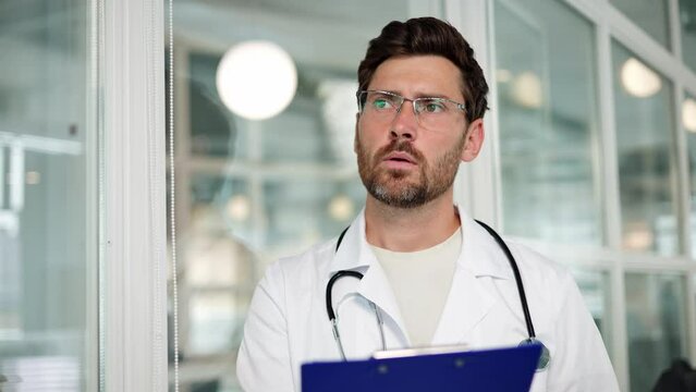 Adult Man Doctor Studying Medical Report Of Patient In Office Room. Male Practitioner Doing Paperwork In Hospital Office. Concentrated Serious Doctor In White Coat, Stethoscope Holding Medical Papers.