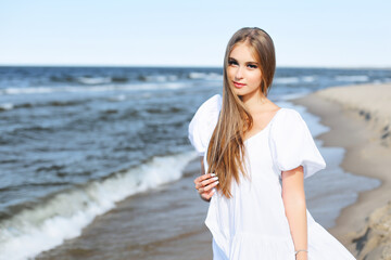 Fototapeta na wymiar Happy, beautiful woman on the ocean beach standing in a white summer dress