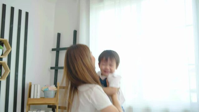 Happy young adult asian mom holding cute adorable child son lifting up standing at bedroom. Cheerful adult mommy playing with cute funny kid baby having fun together, Soft touch, love care