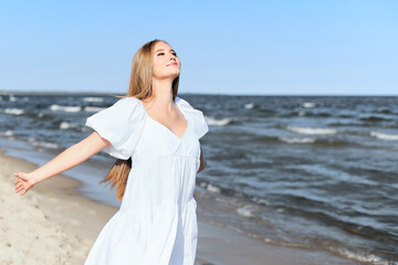 Happy smiling beautiful woman is on the ocean beach in a white summer dress, open arms