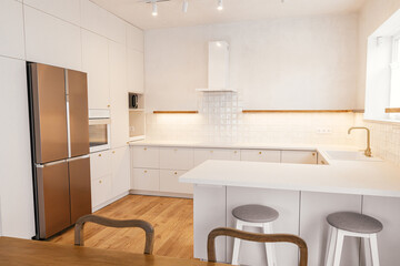 Modern kitchen interior. Stylish white kitchen cabinets with brass knobs, faucet, granite island and appliances in new scandinavian house. Modern minimal kitchen design