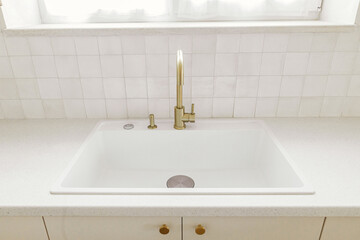 Modern minimal kitchen design. Stylish brass faucet and white granite sink, kitchen cabinets with knobs and granite counter in new scandinavian house.  Modern kitchen interior