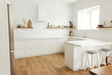Modern minimal kitchen design. Stylish white kitchen cabinets with brass knobs, wooden shelves with utensils and appliances in new scandinavian house. Modern kitchen interior