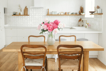 Modern kitchen interior. Beautiful peonies in vase on wooden table on background of stylish white kitchen with appliances in new rustic farmhouse. Minimal kitchen design