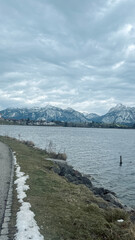 The Hopfensee in winter photographs from a hiking trail on a wooden bridge with dramatic sky and snow covered mountains