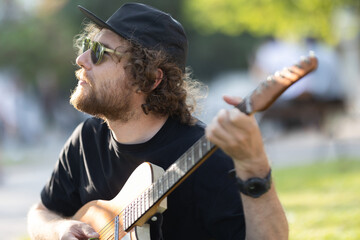 A man hipster wearing hat and sunglasses playing guitar in the park