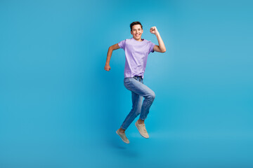 Fototapeta na wymiar Full length portrait of excited young man in t-shirt jumping success running fast isolated over blue background