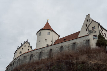 A small white castle in the old town of Füssen photographs in winter with light snow and a park in the foreground