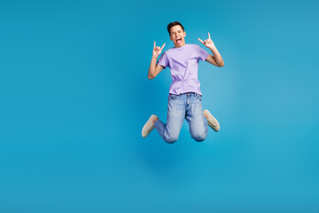 Fototapeta na wymiar Full length photo of excited young man in t-shirt jumping celebrating party horned symbol isolated blue background