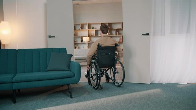 Following Shot of the young smilling Man in the Wheelchair Moving through the room. Male turns and smiles at the camera