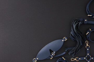 Erotic enjoyment BDSM toy ideas. Top view photo of cuffs, blindfold mask, leather whip on black...