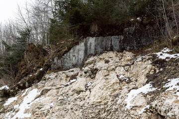 A closeup of a mountain with rocks and trees growing at the top on a slope near town