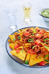 Nachos, Mexican food, tortilla chips with beef and fresh vegetables, with tequila and guacamole dip, on a stone table