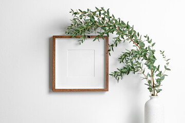 Blank square frame mockup for artwork or print on white wall with eucalyptus plant in vase