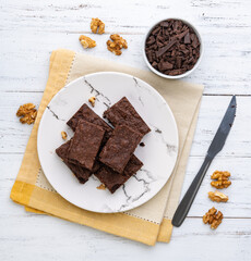 Brownies on a plate with chocolate pieces and walnuts over white wooden table