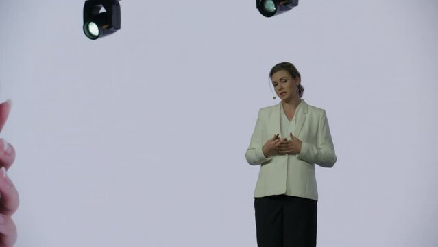 A woman presenter is standing on a well-lit stage in front of a large LED screen showing a hand holding a generic smartphone with green screen. Technology, application or product launch presentation 